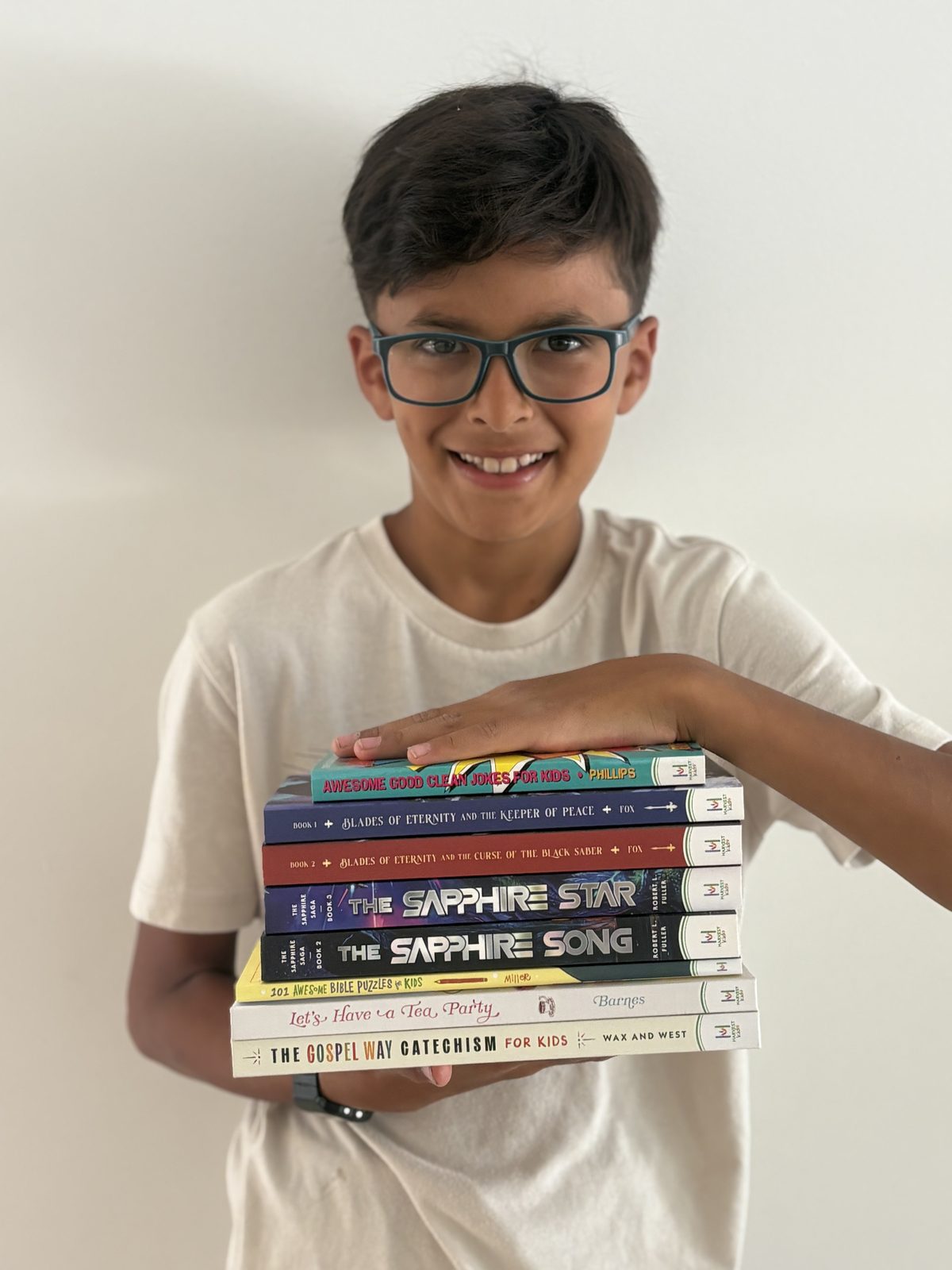 A smiling tween boy in glasses holding a stack of Harvest Kids books against his chest
